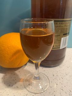 a glass filled with liquid next to an orange on a counter top near a bottle of wine