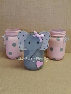 three pink and gray jars with an elephant on them, one has a bow around its neck