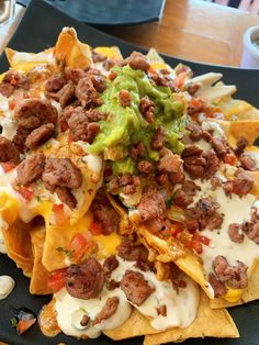 nachos with meat, cheese and guacamole on a black plate