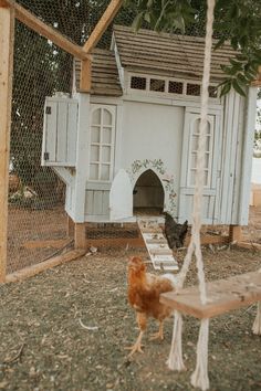 two chickens in a yard with a chicken house and swing set on the other side