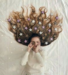 a woman laying on top of a bed with stars in her hair and looking at the camera