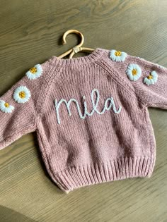 a pink sweater with daisies on it and the word mia written in white letters