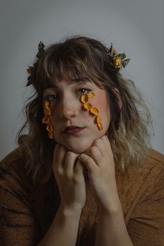 a woman with yellow flowers on her face is looking at the camera while holding her hands to her chin