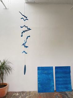 a blue wind chime hanging from the side of a white wall next to a potted plant