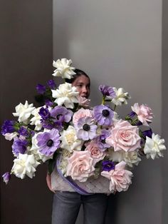 a woman holding a large bouquet of flowers in front of her face while standing next to a wall