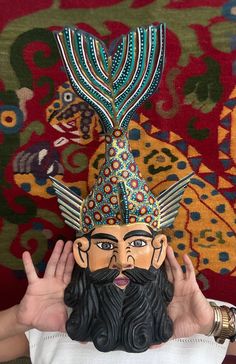 a man is holding up a mask with a long beard and wearing a headdress