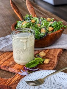 a salad with dressing in a jar on a wooden table next to a white plate