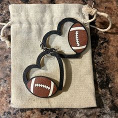 two heart shaped wooden earrings with footballs on them sitting in a bag next to each other