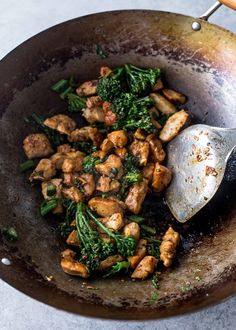 chicken and spinach stir fry in a wok with a wooden spoon on the side