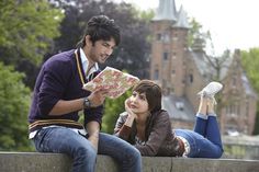 a man and woman sitting on a wall looking at a map with trees in the background