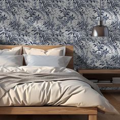 a bed with white sheets and pillows in front of a blue floral wallpaper