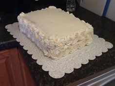 a square white cake sitting on top of a counter next to a glass vase and knife