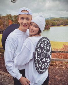 a man and woman standing next to each other in front of a lake