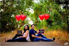 two people sitting on the ground holding signs that say save the date and heart balloons