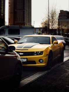 a yellow chevrolet camaro is driving down the street with other cars in the background