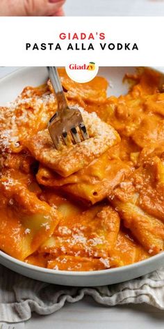 a white bowl filled with pasta and sauce next to a hand holding a fork in it