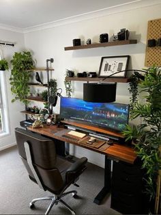 a desk with a computer monitor, keyboard and plant on it in front of a window