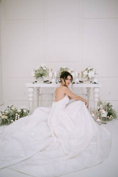 a woman in a white wedding dress sitting on the floor next to a table with flowers and candles