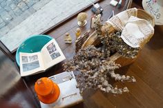 an open book sitting on top of a wooden table next to a basket filled with flowers