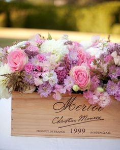 a wooden box filled with pink and white flowers on top of a table covered in cloth