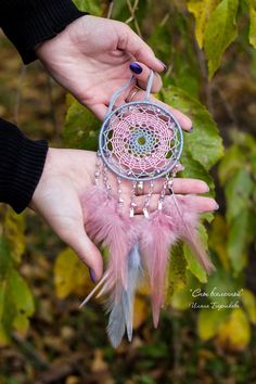 two hands holding a pink and blue dream catcher