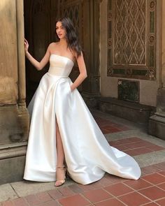 a woman standing in front of a doorway wearing a white dress with high slits