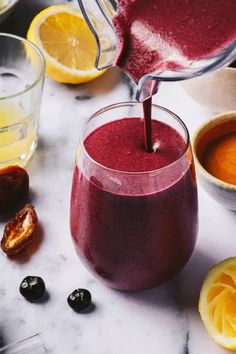 a pitcher pouring liquid into a glass filled with blueberries, oranges and cranberry sauce