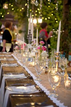 a long table is set with candles, plates and silverware for an elegant dinner