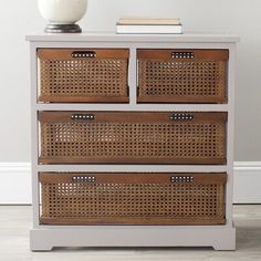 a white dresser with wicker baskets on top and a vase sitting on top of it