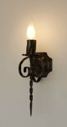 a wall mounted light with a candle on it's side and a hook in the middle