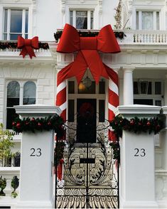 a large red bow on the front door of a white house with christmas decorations around it