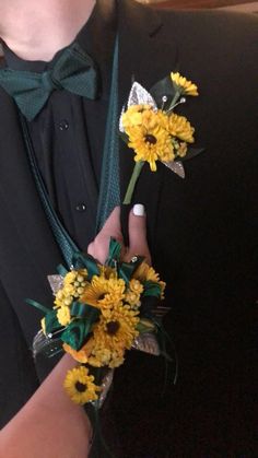 a man in a tuxedo is holding two yellow sunflowers and one green bow tie