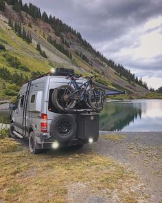 a van parked next to a lake with two bikes on the roof and lights on