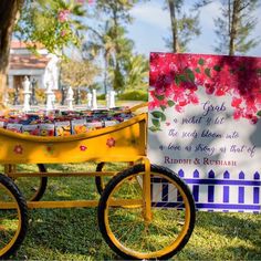 a yellow wheelbarrow with flowers on it next to a sign