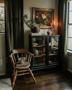 a wooden chair sitting in front of a window next to a painting on the wall