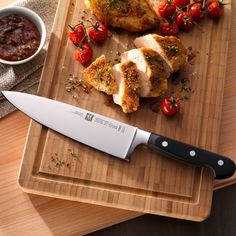 a large knife sitting on top of a cutting board next to some meat and tomatoes