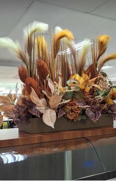 an arrangement of dried flowers and leaves in a vase on a counter at the airport