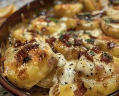 a bowl filled with potatoes covered in cheese and seasoning next to sliced lemon wedges