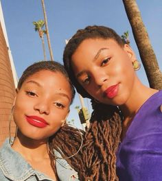 two women standing next to each other with their arms around one another and palm trees in the background