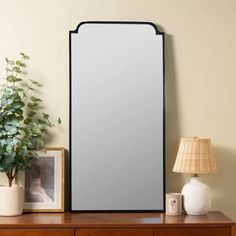 a mirror sitting on top of a wooden dresser next to a lamp and potted plant