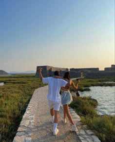 a man and woman walking down a path next to a body of water