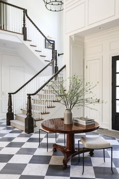 a room with a checkered floor, stairs and table in the center surrounded by chairs