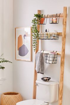 a white toilet sitting next to a wooden ladder in a bathroom with plants on the wall