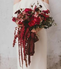 a woman in white dress holding a bouquet of flowers with red ribbons on her arm