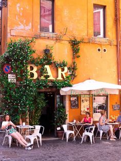 people sitting at tables in front of an orange building with ivy growing on the wall