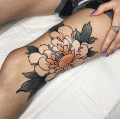 a woman's leg with a flower tattoo on the thigh and her hand resting on top of it