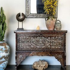 an old wooden dresser sitting in front of a mirror and potted plant on top of it