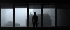 the silhouette of a person standing in front of large windows on a foggy day