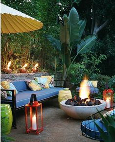 an outdoor seating area with fire pit and umbrellas in the background, surrounded by greenery