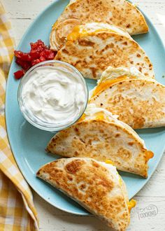 several quesadillas on a blue plate with sour cream